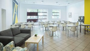 Uma ampla área de refeições com várias mesas e cadeiras, um sofá cinzento e uma pequena mesa com uma planta.