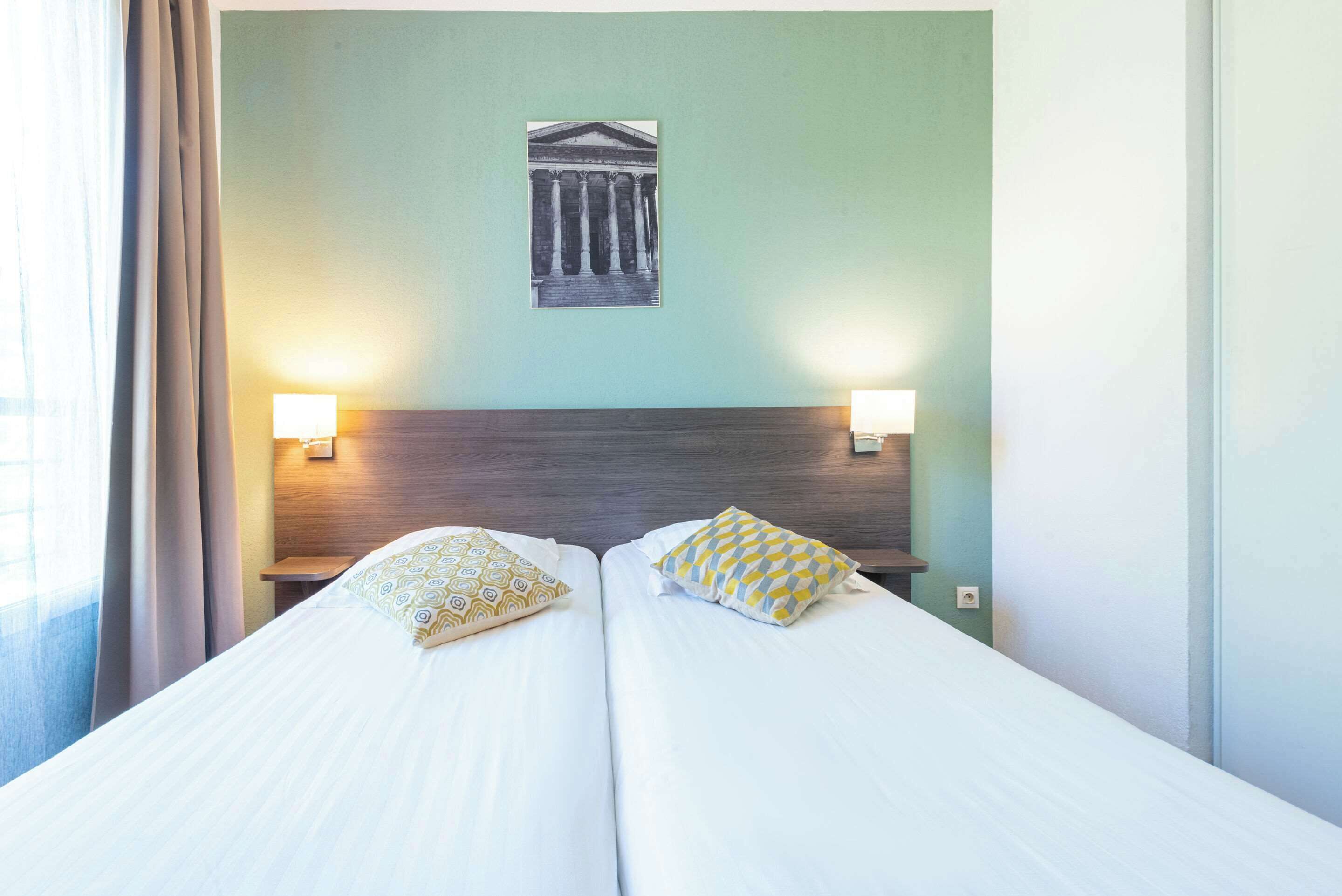 A double bed with two pillows, a nightstand, a wall-mounted lamp, and a framed picture above the bed.