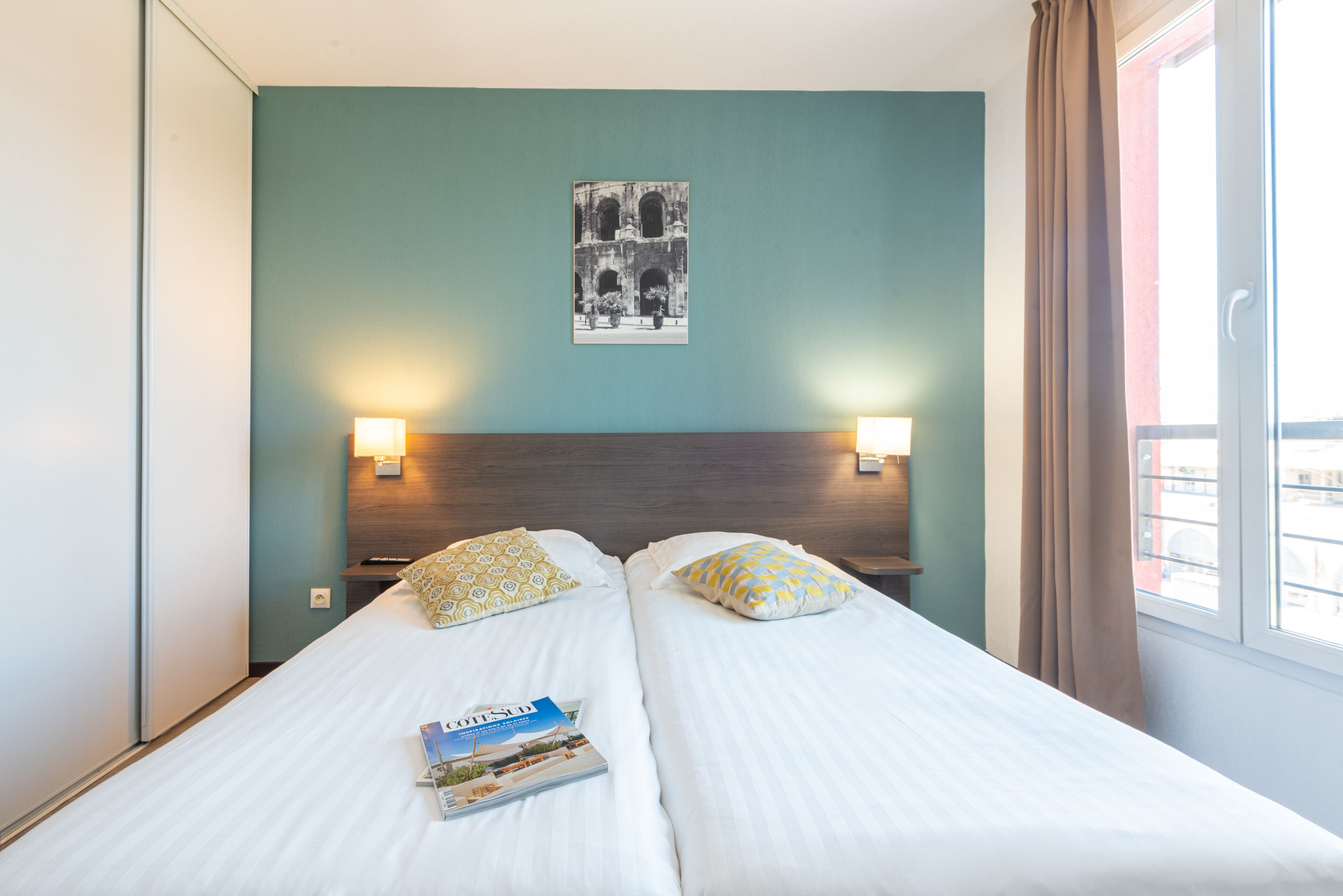 Ett hotellrum med två sängar, en inramad tavla på väggen och ett fönster med gardiner.
