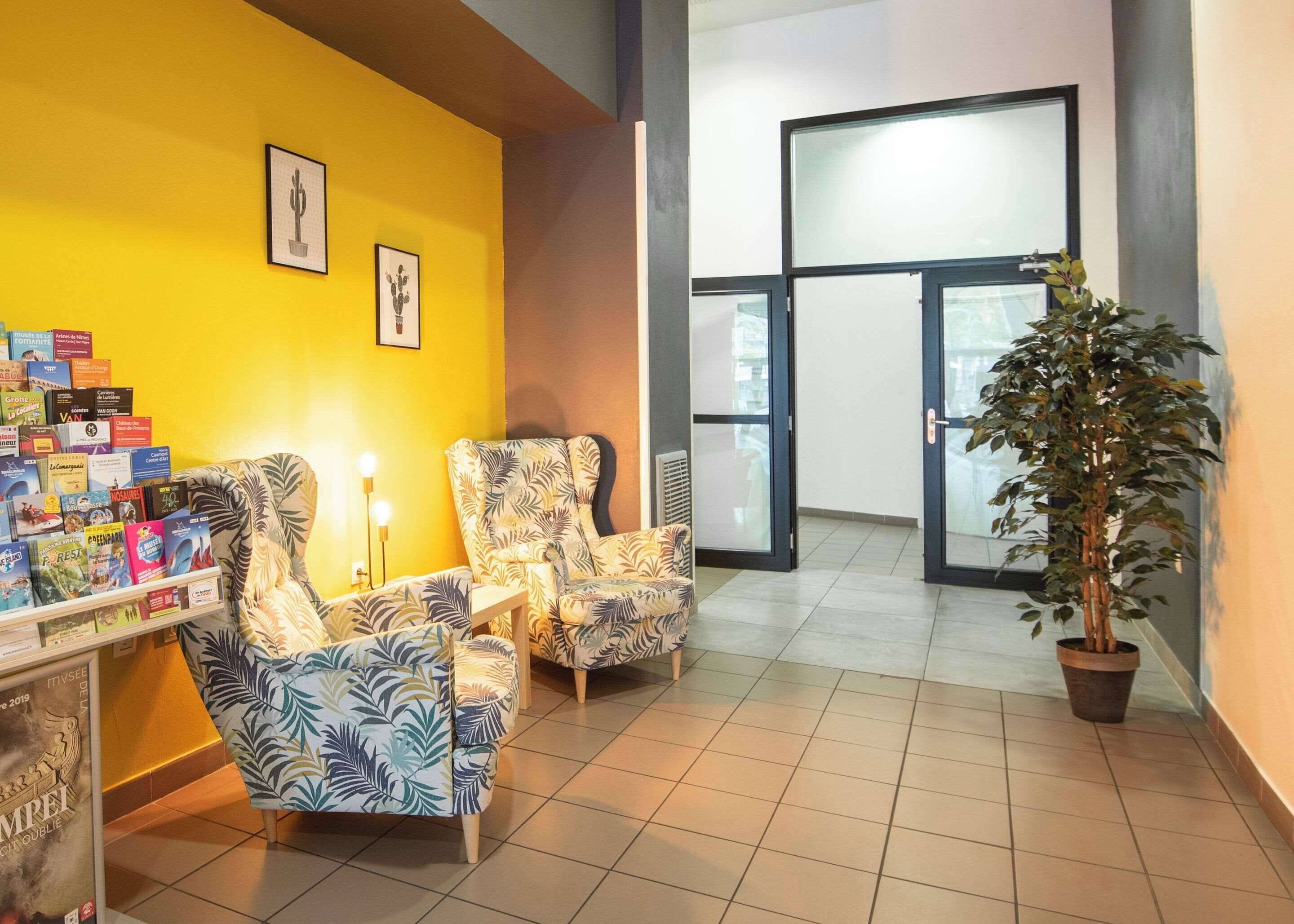 A reception area with a yellow wall, two patterned armchairs, a small table with a lamp, and a potted plant.