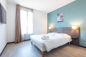 Une chambre d’hôtel avec un lit, une table de chevet, un téléviseur fixé au mur et une fenêtre avec des rideaux.