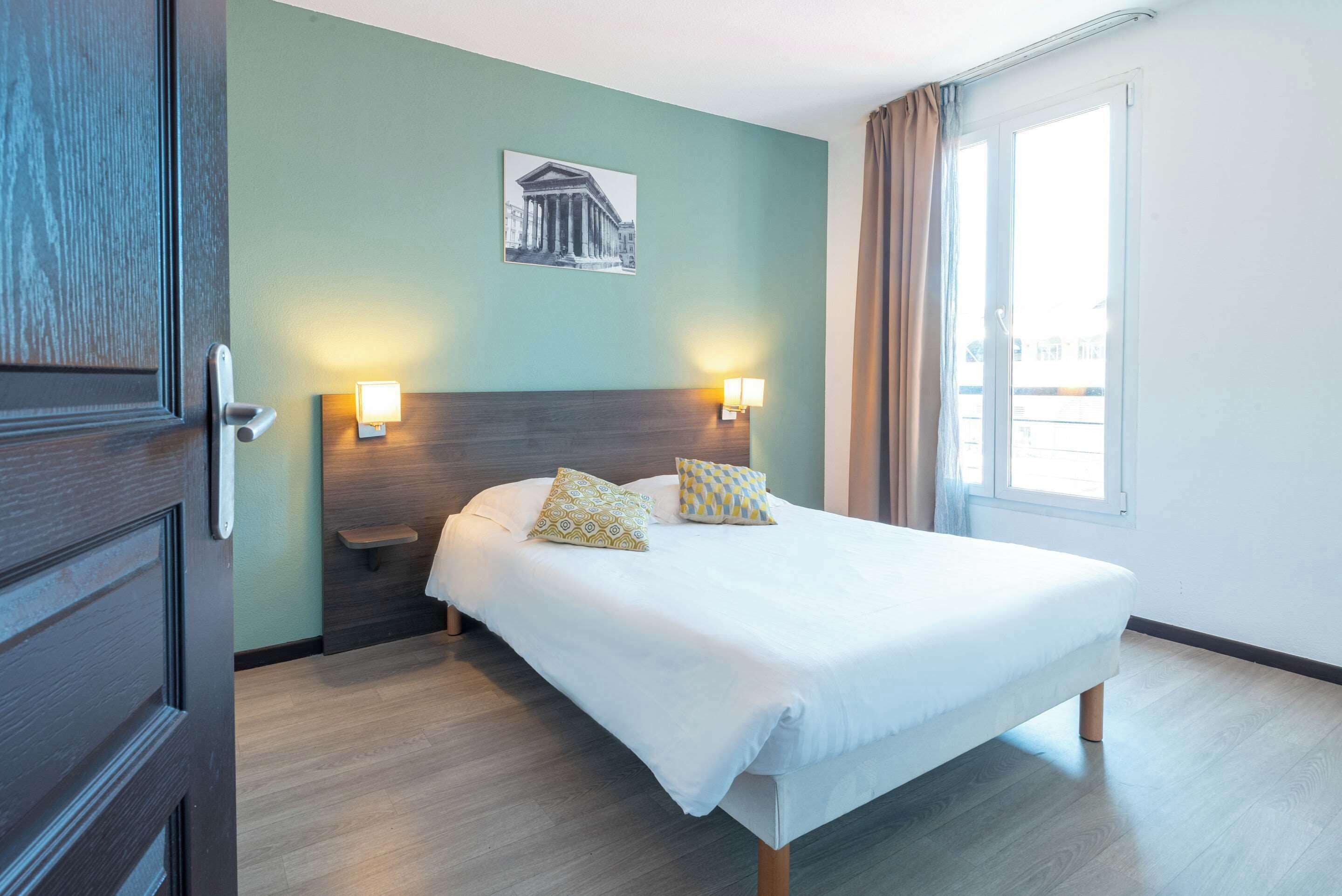 A hotel room with a large bed, two bedside lamps, a nightstand, a framed picture on the wall, and a window with curtains.