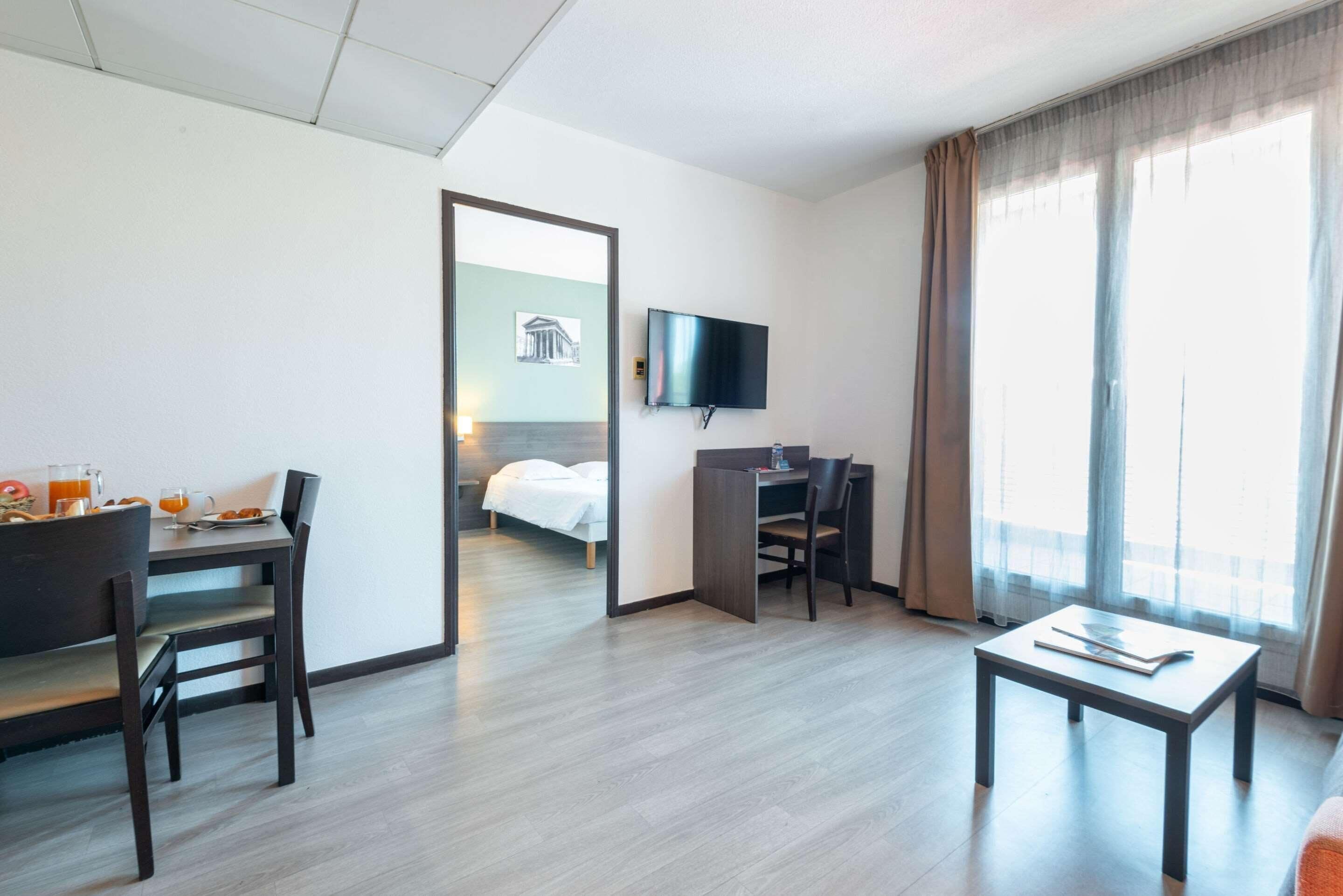 A hotel room with a bed, a desk, a chair, a table, a TV, and a window with curtains.