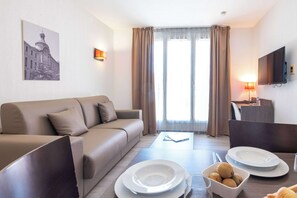 Una habitación de hotel moderna con sofá, mesa de comedor y televisión.