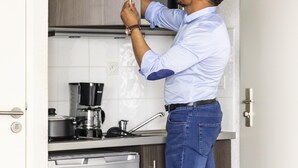 Eine Person installiert einen Schrank in einer Küche, in der ein Kaffeeautomat und ein Geschirrspüler stehen.