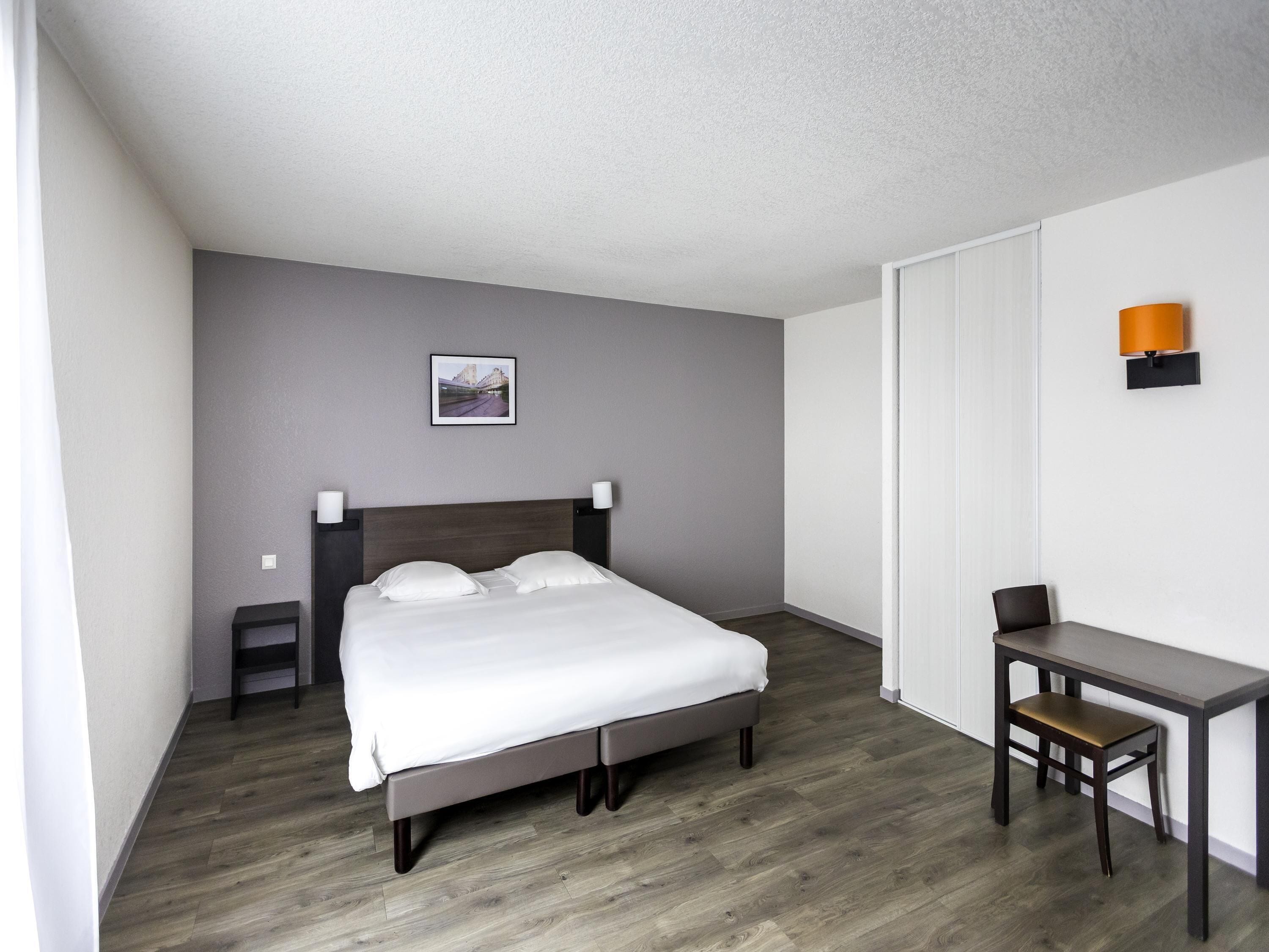 A hotel room with a bed, bedside tables, a desk, and a chair.