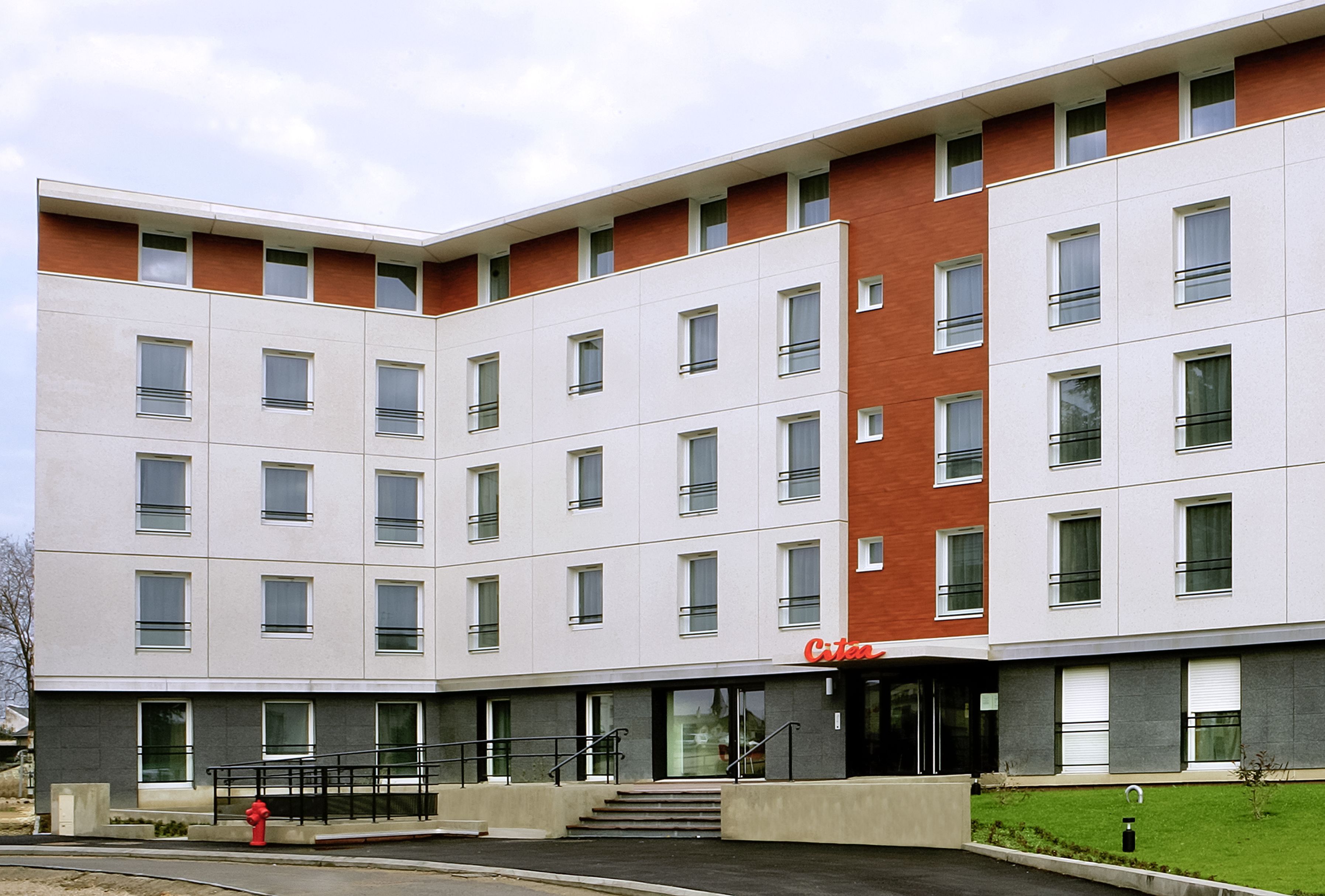 A multi-story hotel with a modern design, featuring a mix of white and red brick facades, large windows, and a visible entrance with steps leading up to the door.