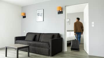 Ett modernt hotellrum med en grå soffa, ett litet bord och en säng.