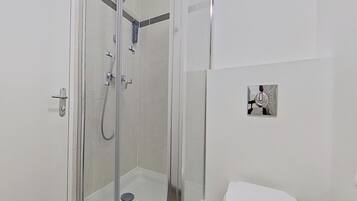 Un baño moderno con ducha de vidrio, inodoro y un lavamanos pequeño fijado a la pared.