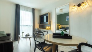 Ein modernes Wohnzimmer mit einer Couch, einem runden Esstisch und Stühlen. Ein Flachbildfernseher ist an der Wand angebracht, und ein kleiner Beistelltisch trägt eine Vase und ein Tablett.