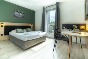 Quarto de hotel moderno com uma cama grande, uma mesa de jantar e vista para o exterior.