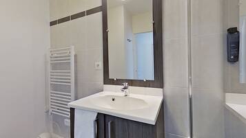 Un baño con lavabo blanco, espejo, toallero y zona de ducha.