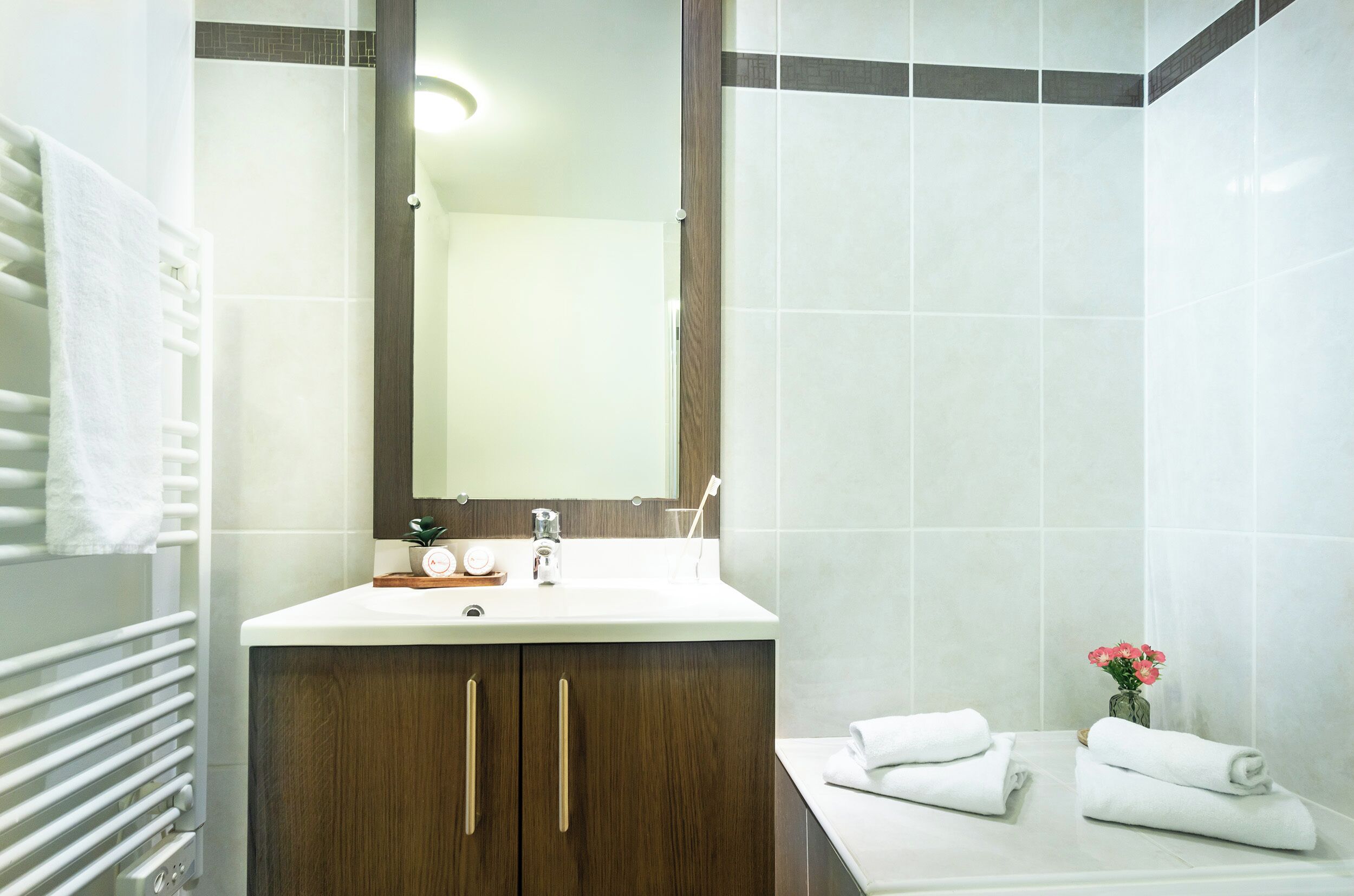 Un baño moderno con un lavamanos blanco, muebles de madera, un espejo grande y un perchero para toallas.