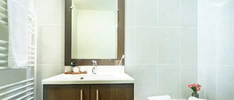 Un baño moderno con un lavamanos blanco, muebles de madera, un espejo grande y un perchero para toallas.