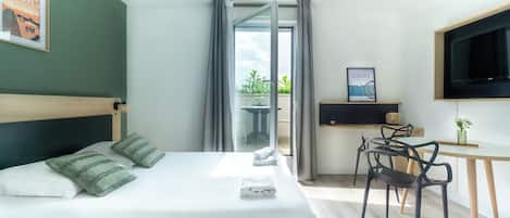 A modern hotel room with a bed, a desk, a chair, a TV, and a balcony with curtains.