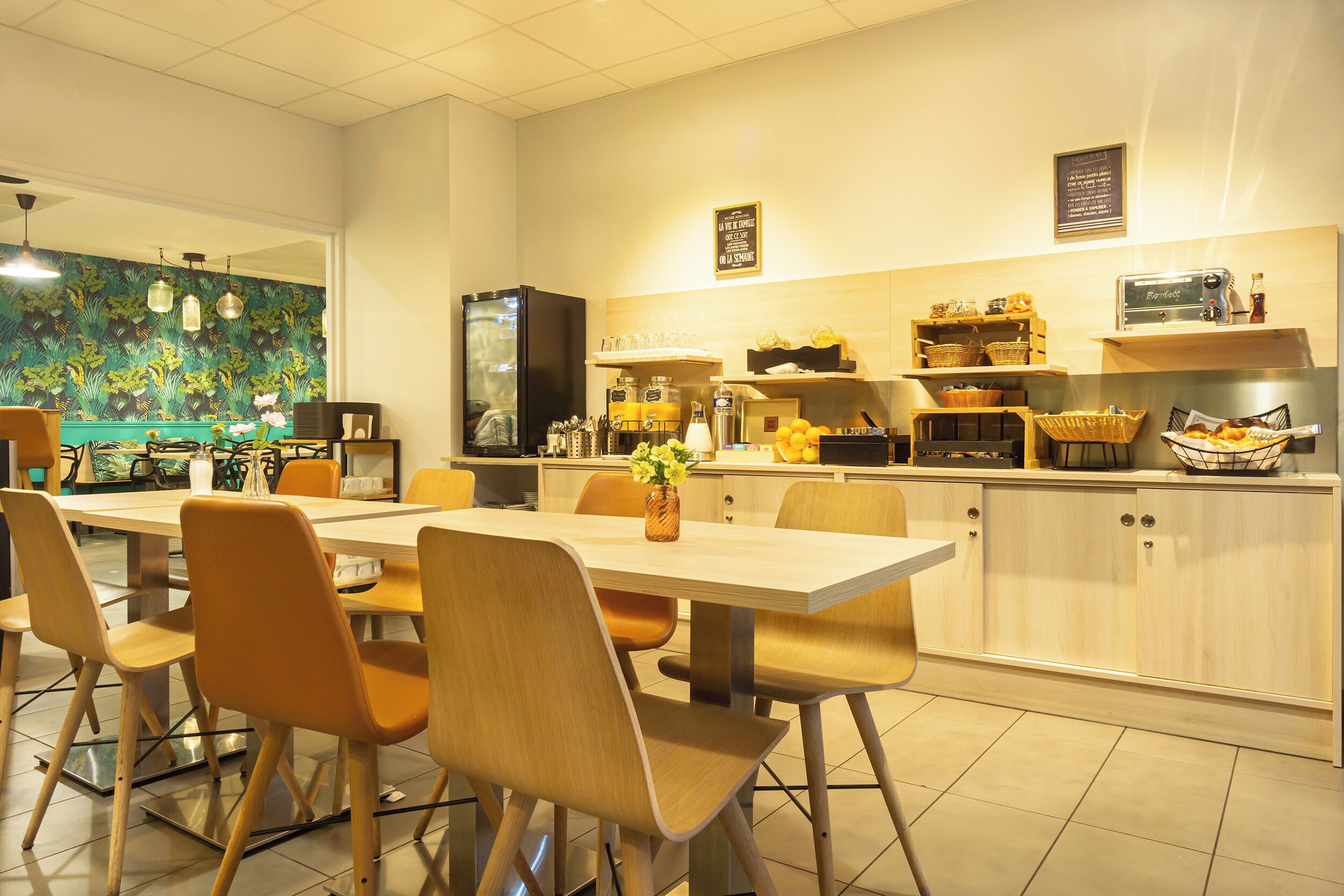 A modern kitchen with a dining area, featuring a long table, chairs, and various kitchen appliances.