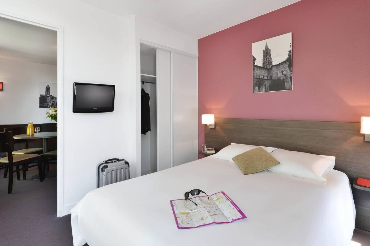 A hotel room with a bed, a television, a map, and a picture on the wall.