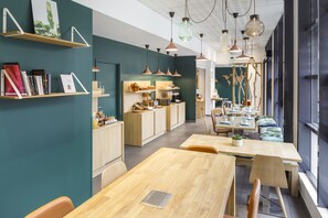 Un comedor moderno y bien iluminado con mesas y sillas de madera, una zona de cocina con armarios de madera e iluminación colgante.