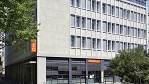 Un edificio moderno con una fachada de ventanas enrejadas, techo plano y un cartel que dice 'adaqio access'.