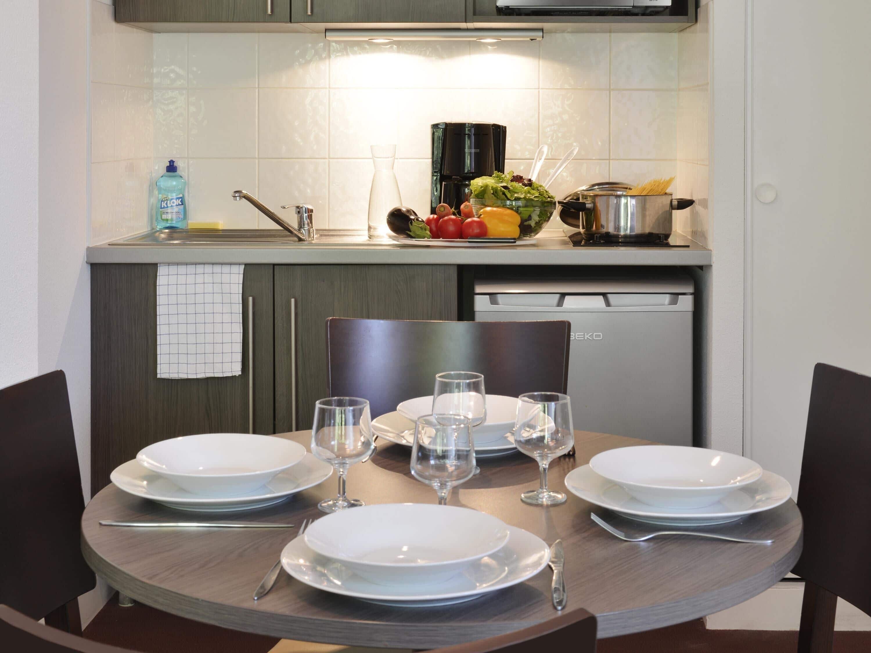 Une cuisine moderne avec une table à manger mise pour quatre personnes, équipée d’assiettes, de verres et de couverts.