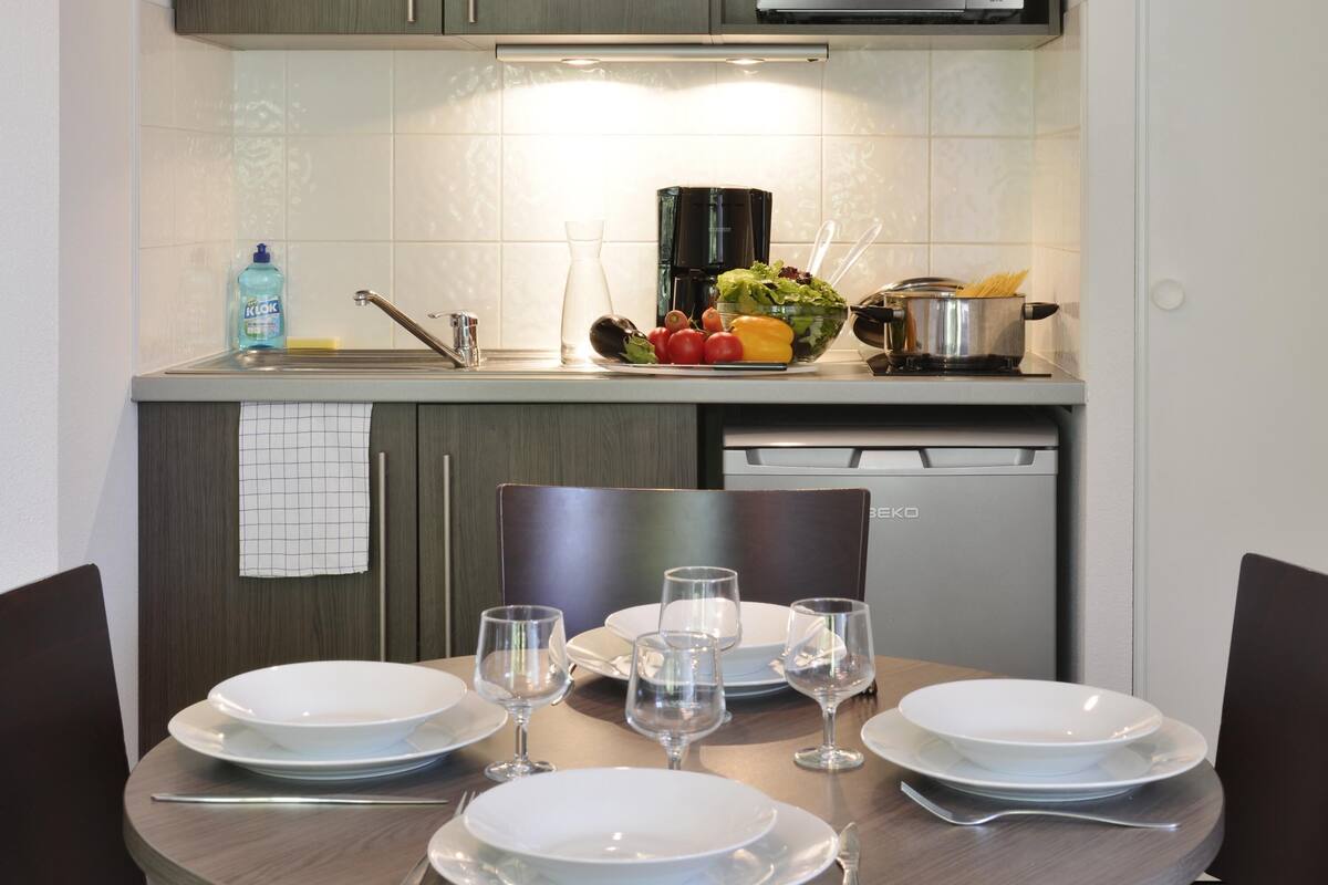 A modern kitchen with a dining table set for four, equipped with plates, glasses, and cutlery.