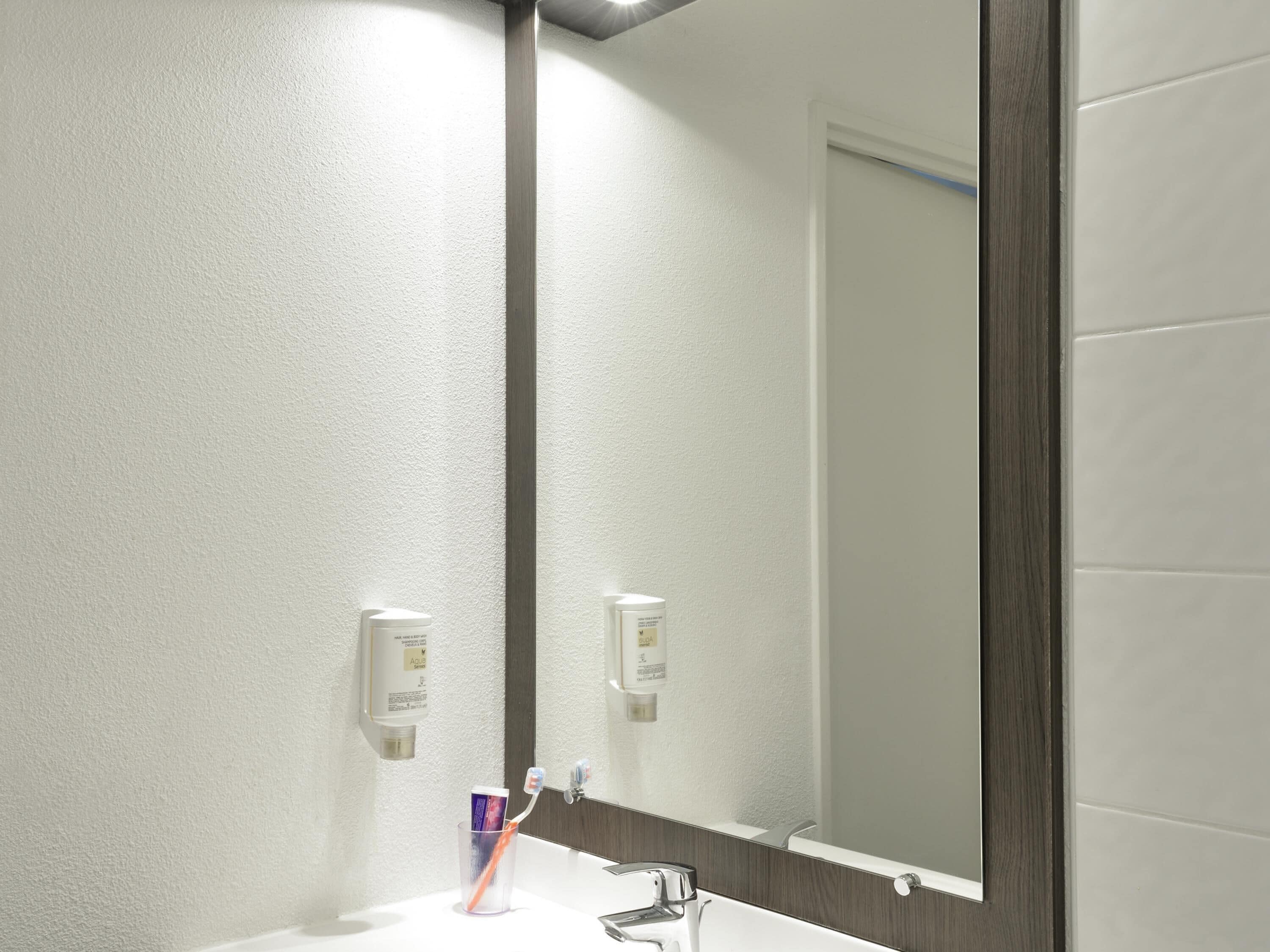 Ein Badezimmer mit einem weißen Waschbecken, einem Spiegel und zwei Seifenspendern.