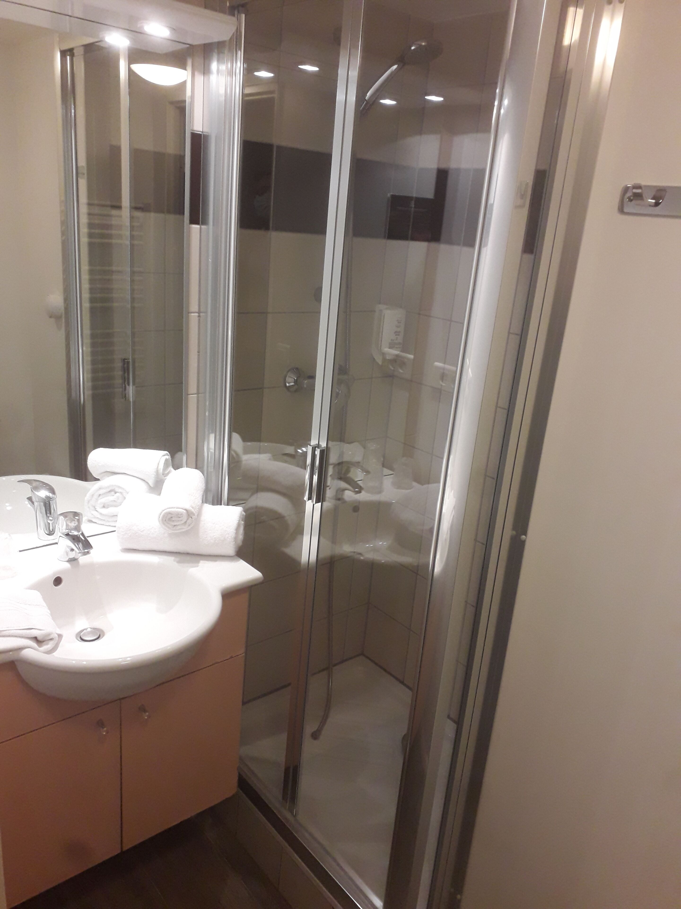 A modern bathroom with a glass-enclosed shower, a white sink, and neatly folded towels on the counter.