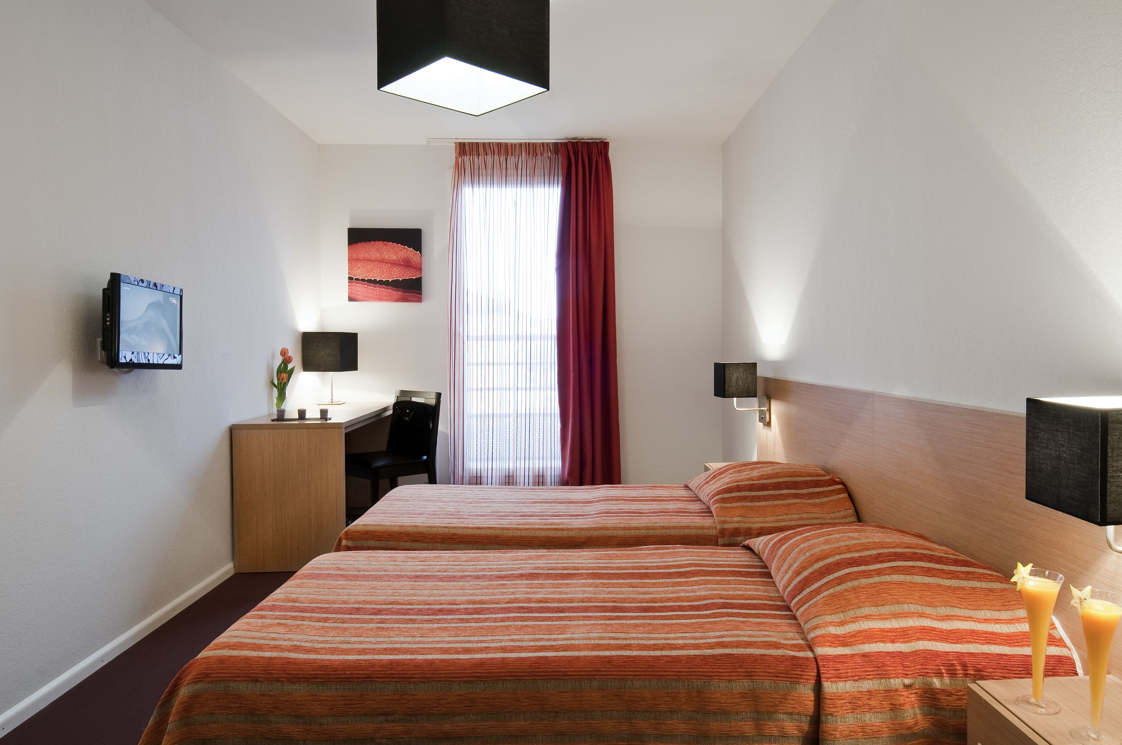 A hotel room with two beds, a desk, a TV, and a window with curtains.
