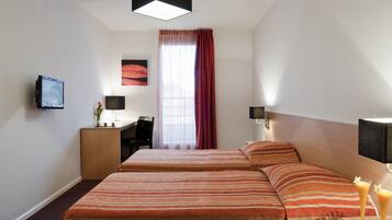 A hotel room with two beds, a desk, a TV, and a window with curtains.