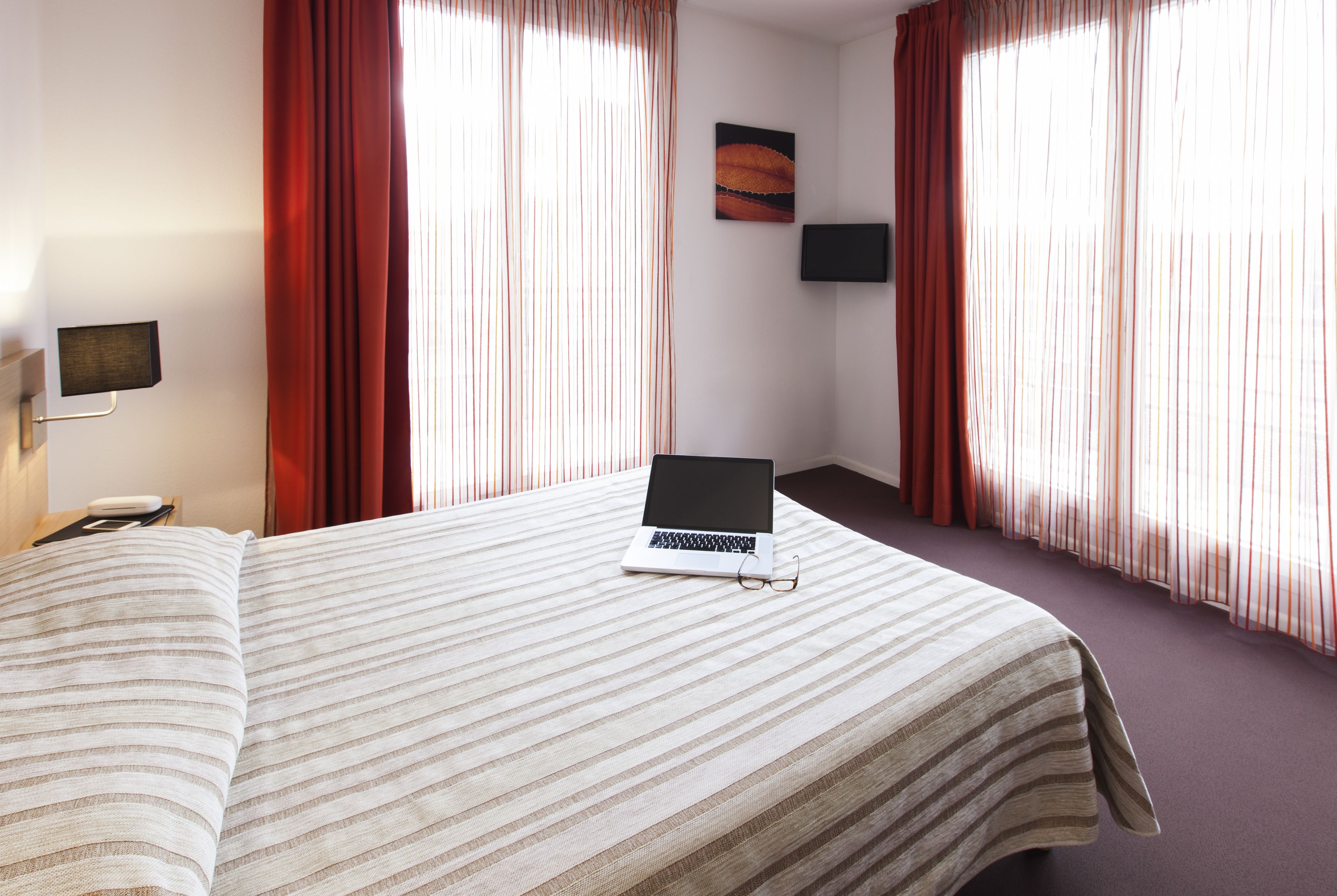 Ein Hotelzimmer mit einem Bett, einem Laptop, einem Fernseher und Vorhängen.