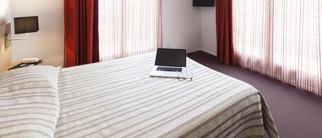 Ein Hotelzimmer mit einem Bett, einem Laptop, einem Fernseher und Vorhängen.