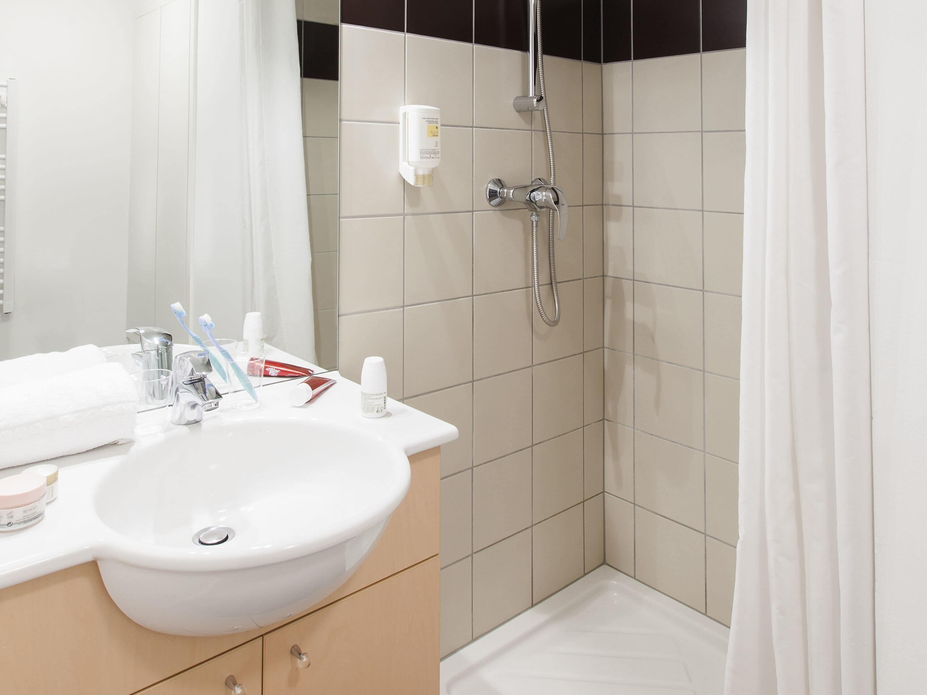 Un baño con lavamanos, espejo, ducha y artículos de aseo.