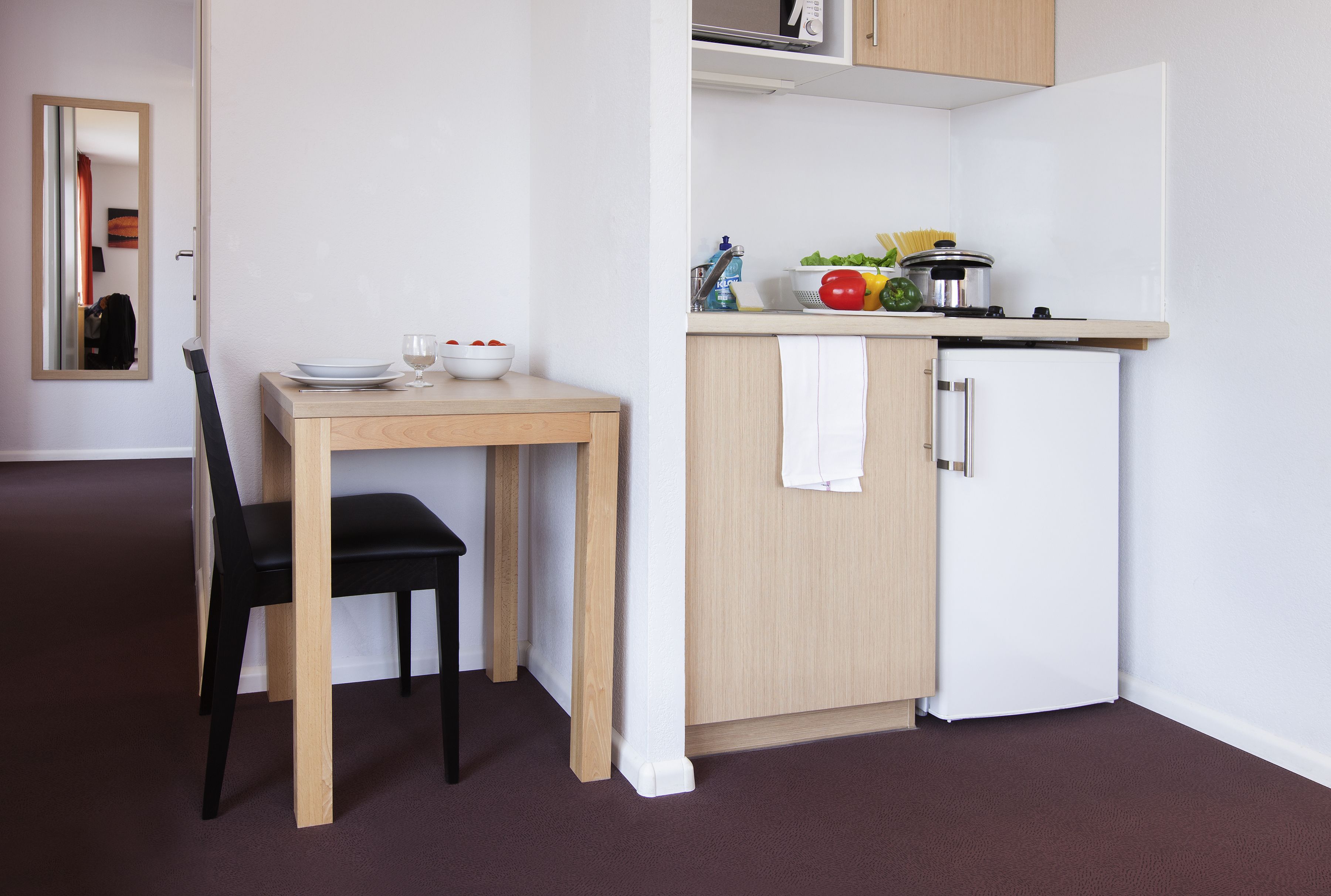 A compact kitchen with a dining table and chair, a microwave, and a sink.