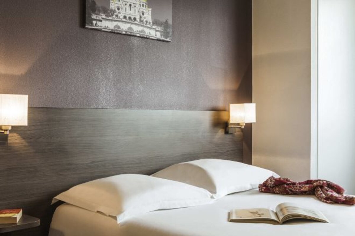 Een hotelkamer met een bed, twee bedlampen, een boek en een aan de muur hangend schilderij.