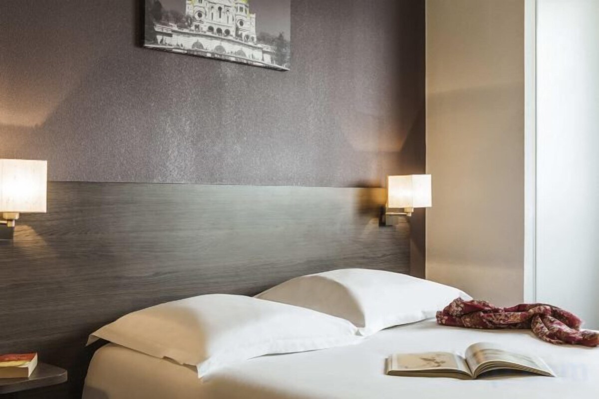 Une chambre d’hôtel avec un lit, deux lampes de chevet, un livre et un tableau accroché au mur.