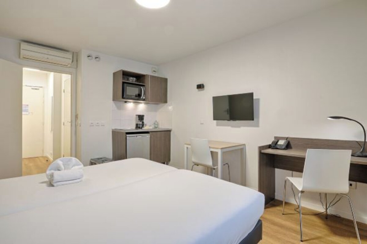 Een hotelkamer met een bed, een bureau, een stoel, een magnetron, een televisie en een kleine kitchenette.