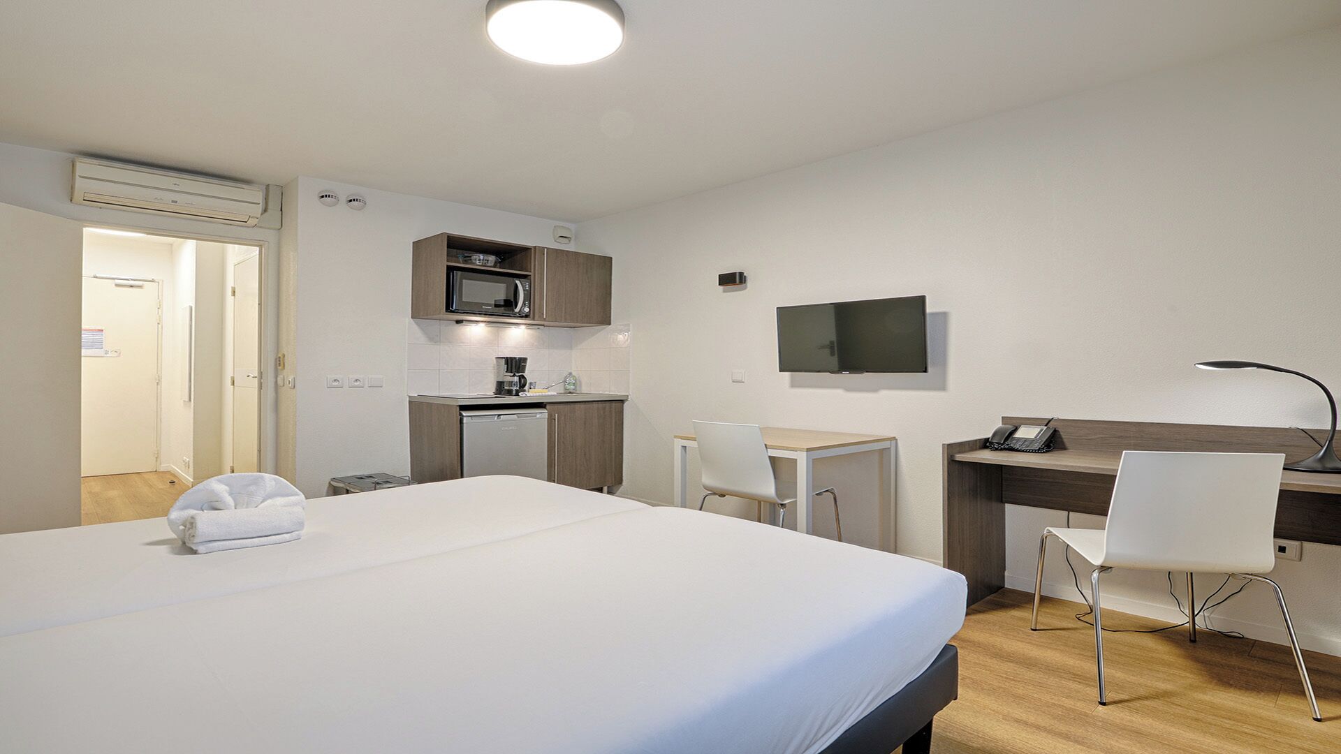 A hotel room with a bed, a desk, a chair, a microwave, a coffee maker, and a TV.