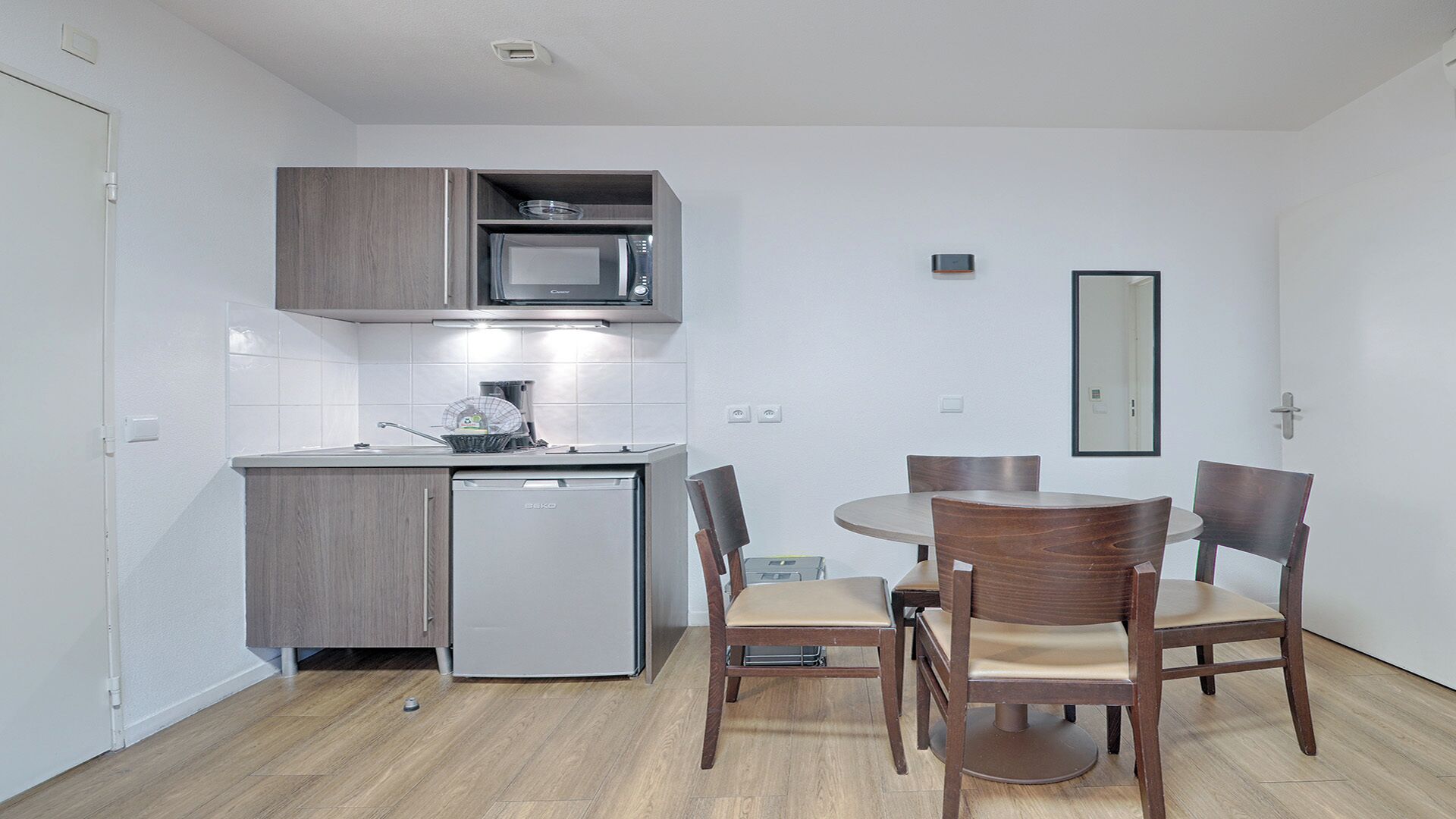 Una cocina compacta con microondas, lavabo y un refrigerador pequeño. Hay una mesa de comedor con cuatro sillas.