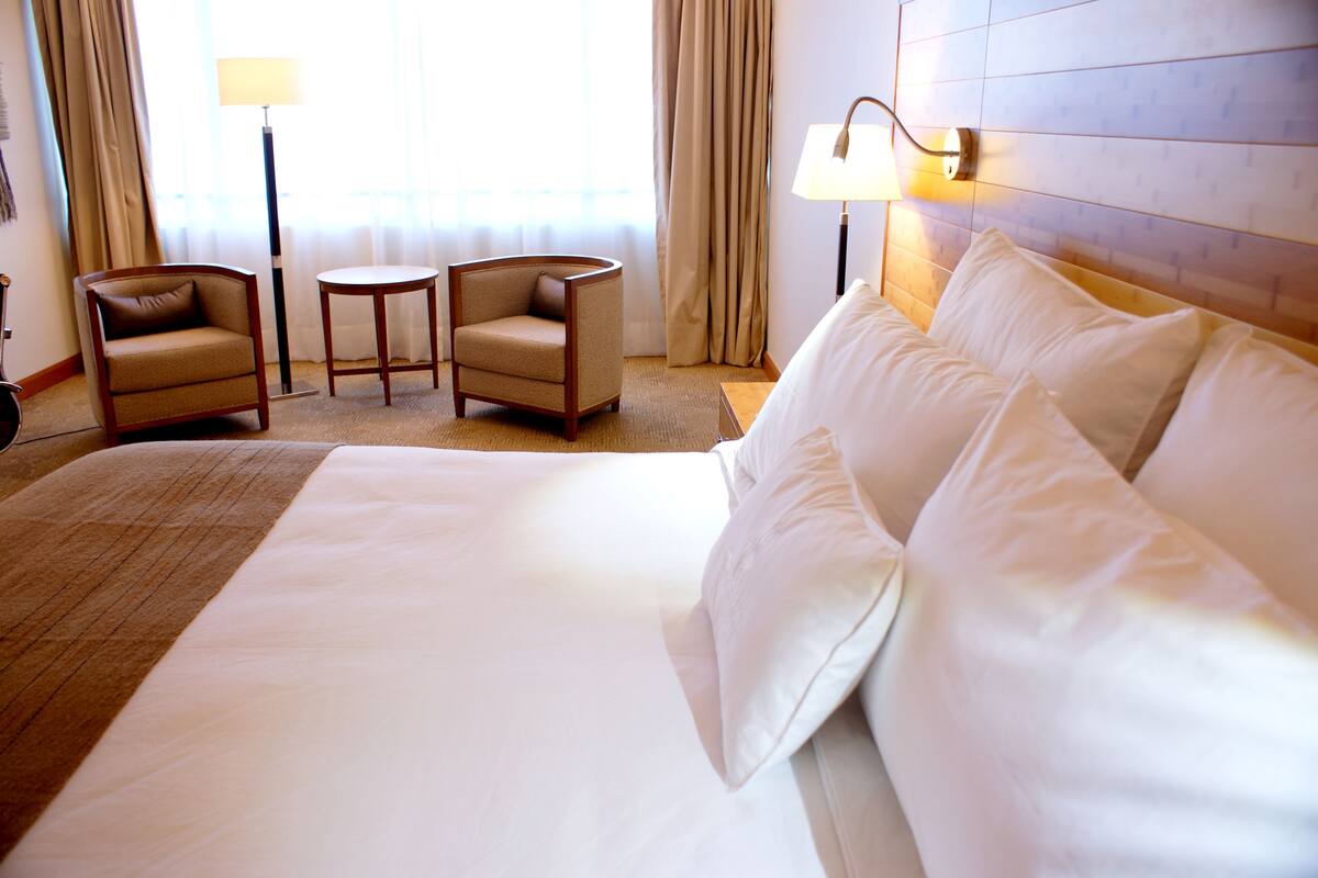 A hotel room with a large bed, two armchairs, a small table, and two lamps.