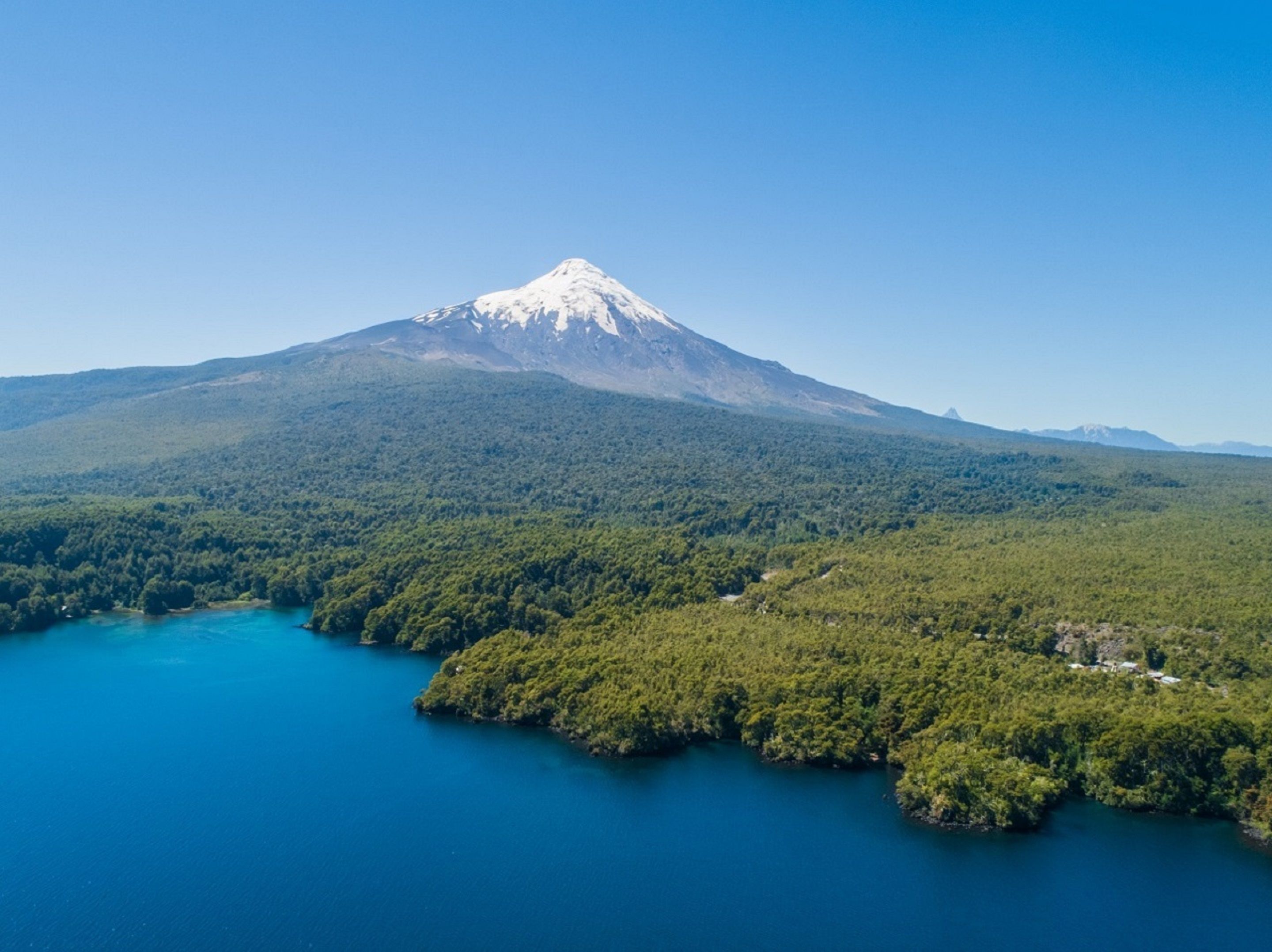 Una montaña con un lago en primer plano y una zona boscosa al fondo.