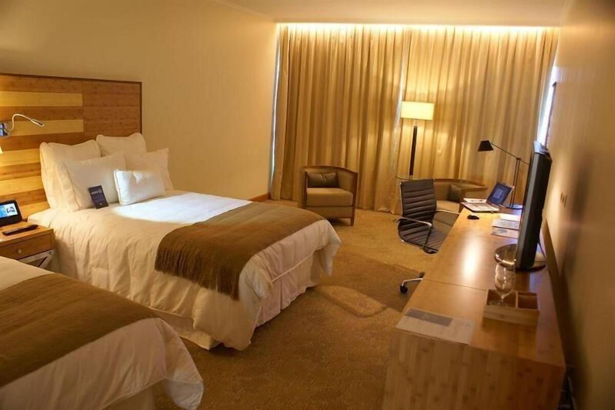 A hotel room with two beds, a desk, a chair, a TV, and a curtain.