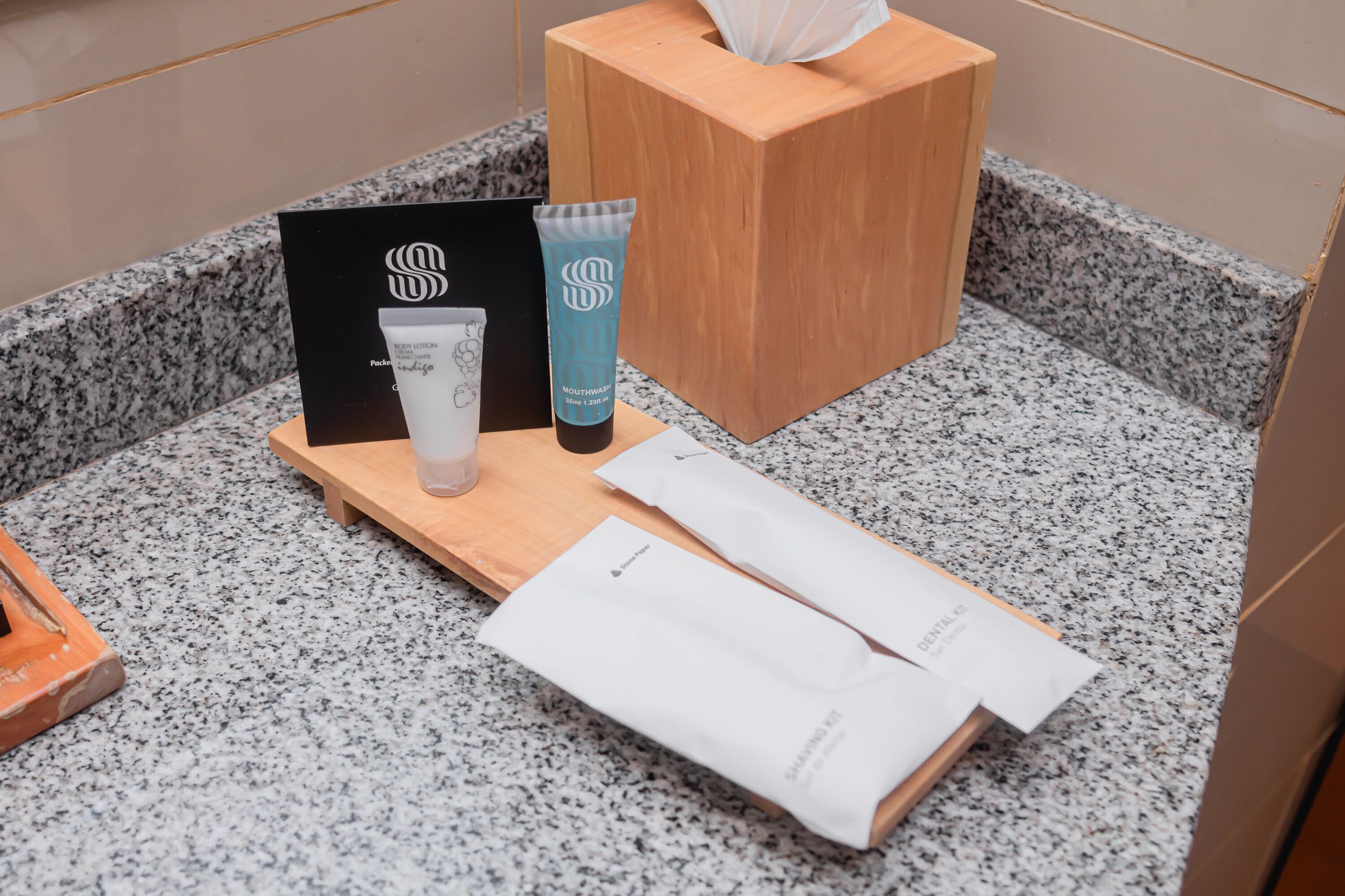 Una encimera de baño con una caja de pañuelos, una tarjeta negra, un tubo de pasta de dientes y un kit de higiene bucal.