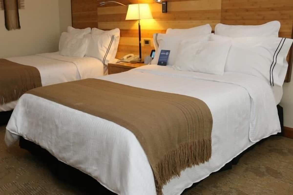 A hotel room with two beds, a wooden headboard, a nightstand with a lamp, and a telephone.