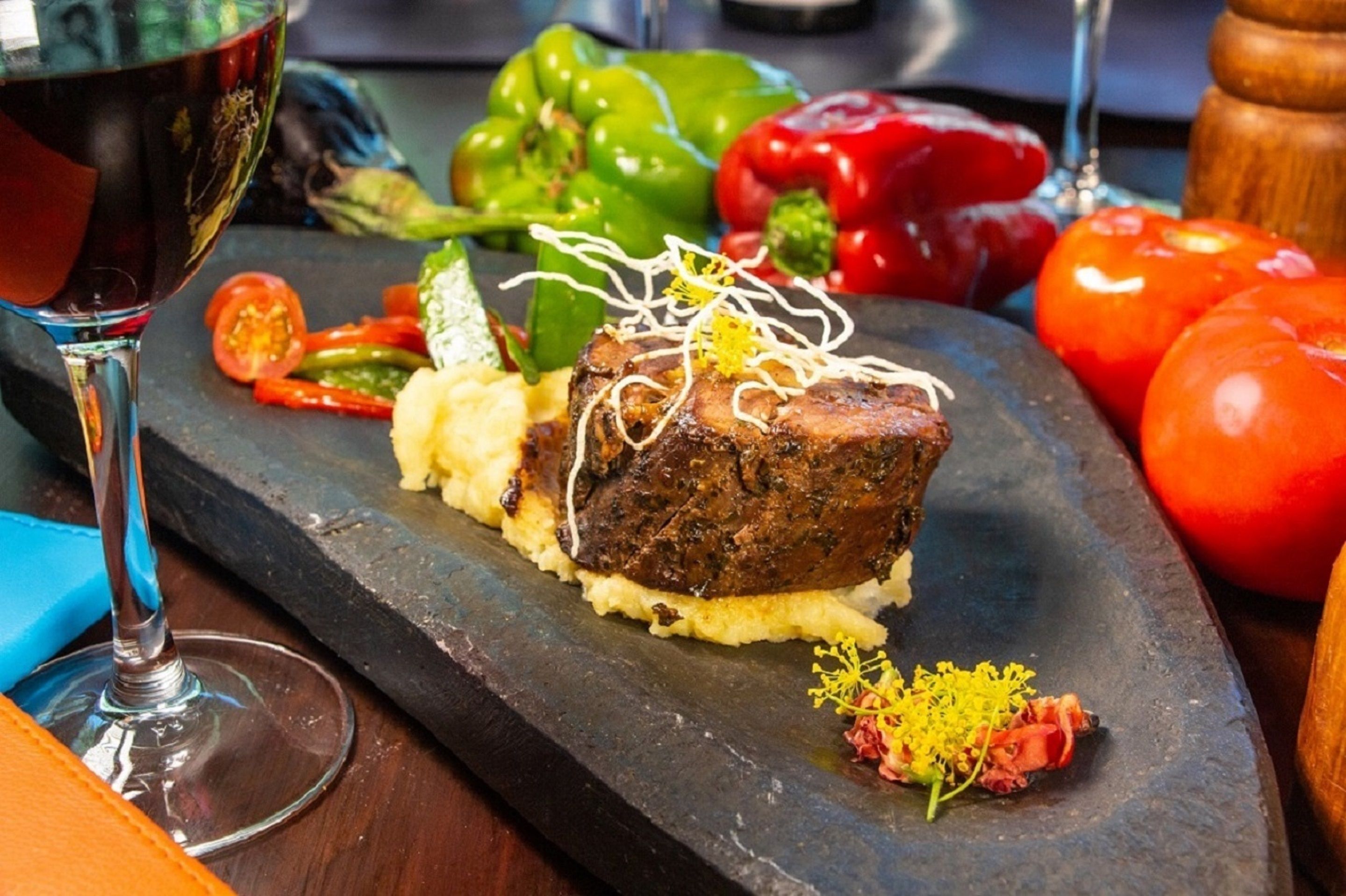 A steak with garnish on a slate plate, accompanied by vegetables and a glass of red wine.