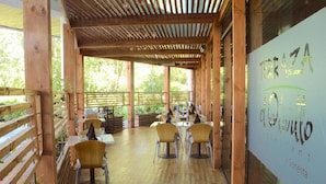 An outdoor dining area with wooden tables and chairs, a pergola overhead, and a view of greenery. - Sonesta Hotel Osorno (Osorno)