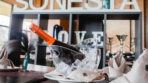 A bottle of champagne in a glass container with ice cubes, placed on a table with a placemat. - Sonesta Hotel Osorno (Osorno)