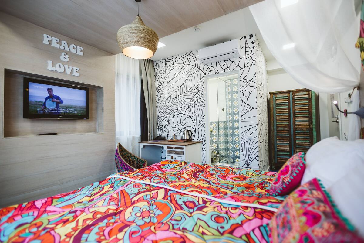 A bedroom with a colorful bedspread, a television mounted on the wall, and a decorative wall with the words "PEACE & LOVE".