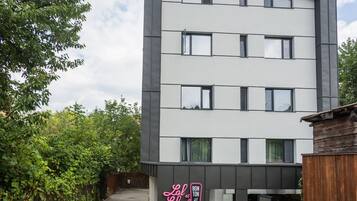 A modern building with a paved courtyard, outdoor seating, and a neon sign.