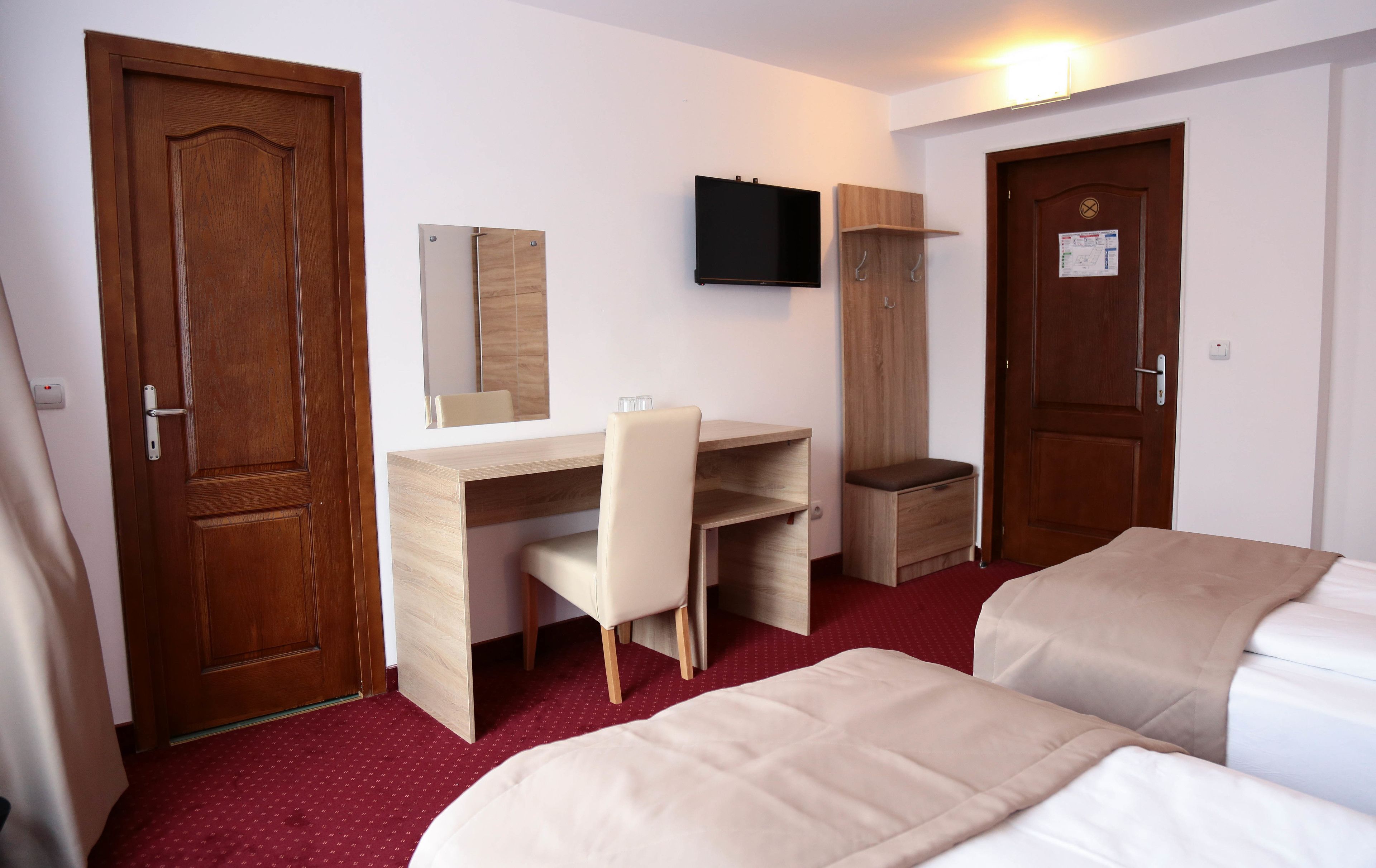 A hotel room with a wooden desk, a chair, a TV mounted on the wall, and two beds.