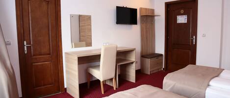 Una habitación de hotel con un escritorio de madera, una silla, un televisor montado en la pared y dos camas.